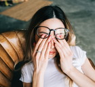 Young woman rubs her eyes after using glasses. Eye pain or fatigue concept.