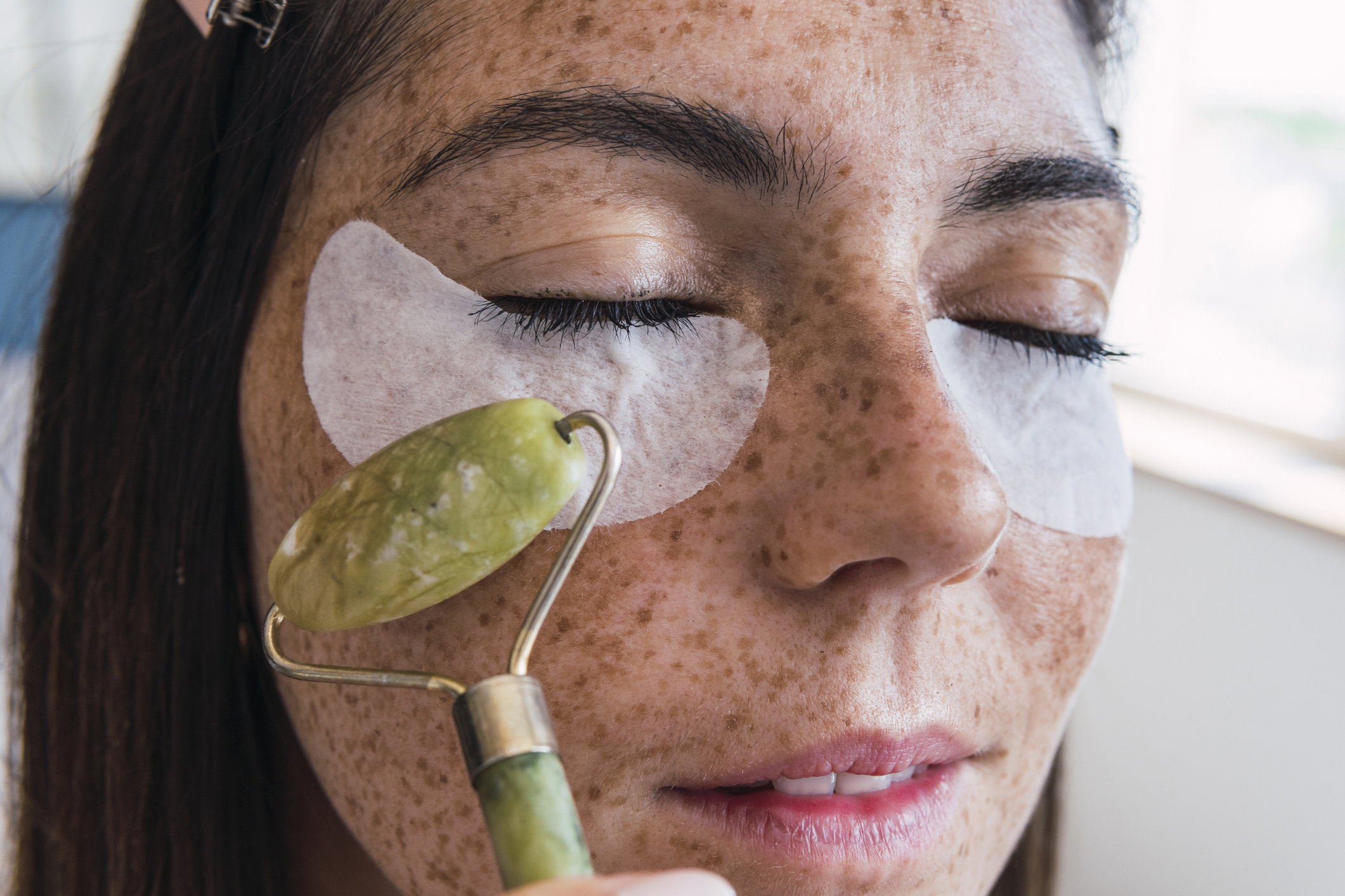Woman with freckle face massaging using jade stone roller
