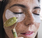 Woman with freckle face massaging using jade stone roller