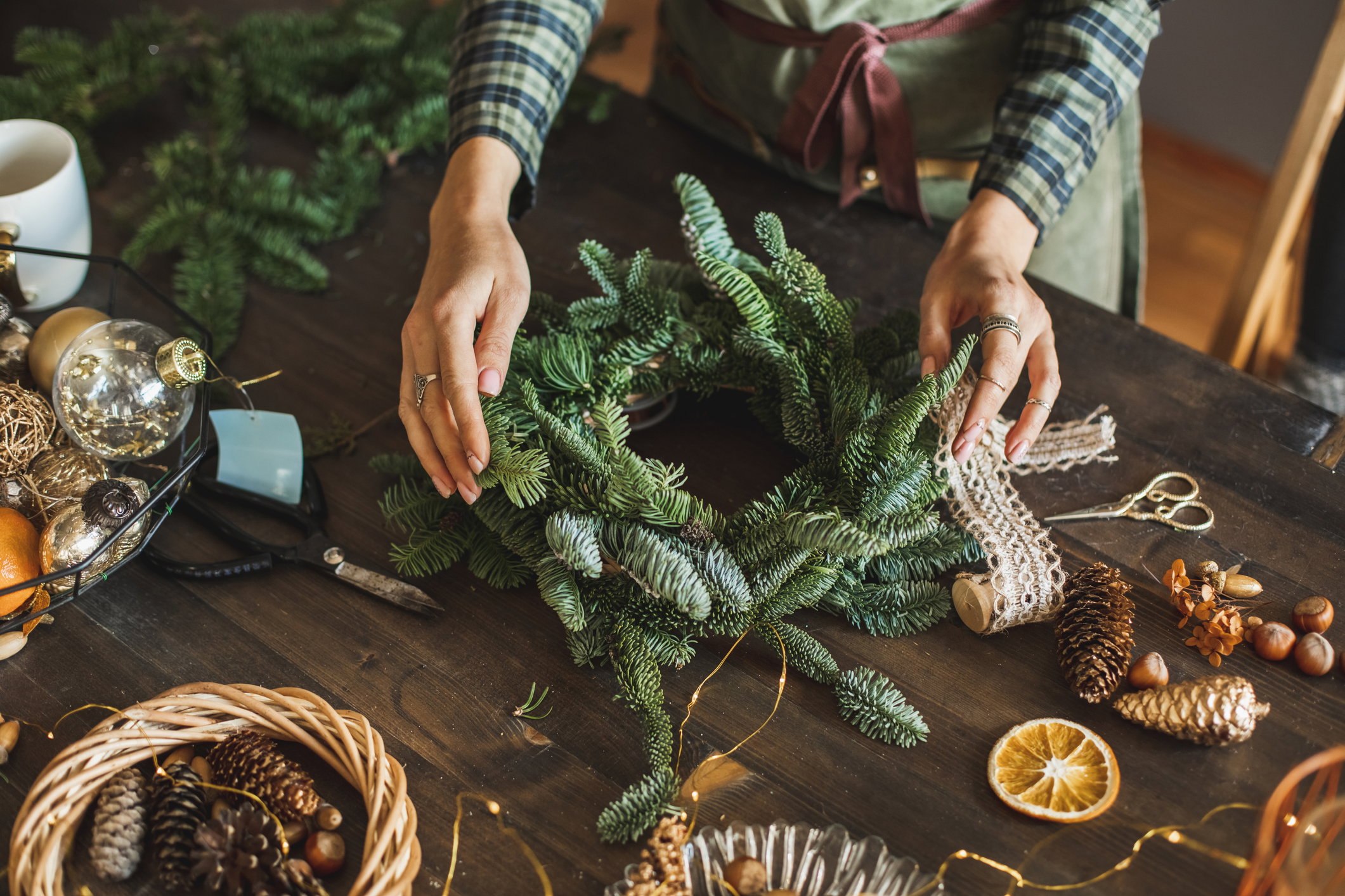 Beautiful woman making Christmas wreath using fresh pine branches and festive decorations.