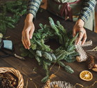 Beautiful woman making Christmas wreath using fresh pine branches and festive decorations.