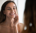 Smiling Latin woman look in bath mirror clean face
