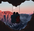 Couple on swing contemplating the mountains in a romantic view with heart shape.