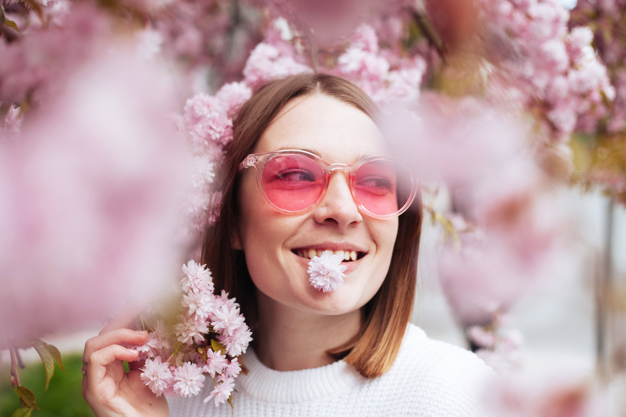 Spring portrait of young woman standing under blossoming pink tree of sakura in park outdoors
