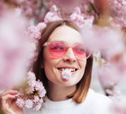Spring portrait of young woman standing under blossoming pink tree of sakura in park outdoors