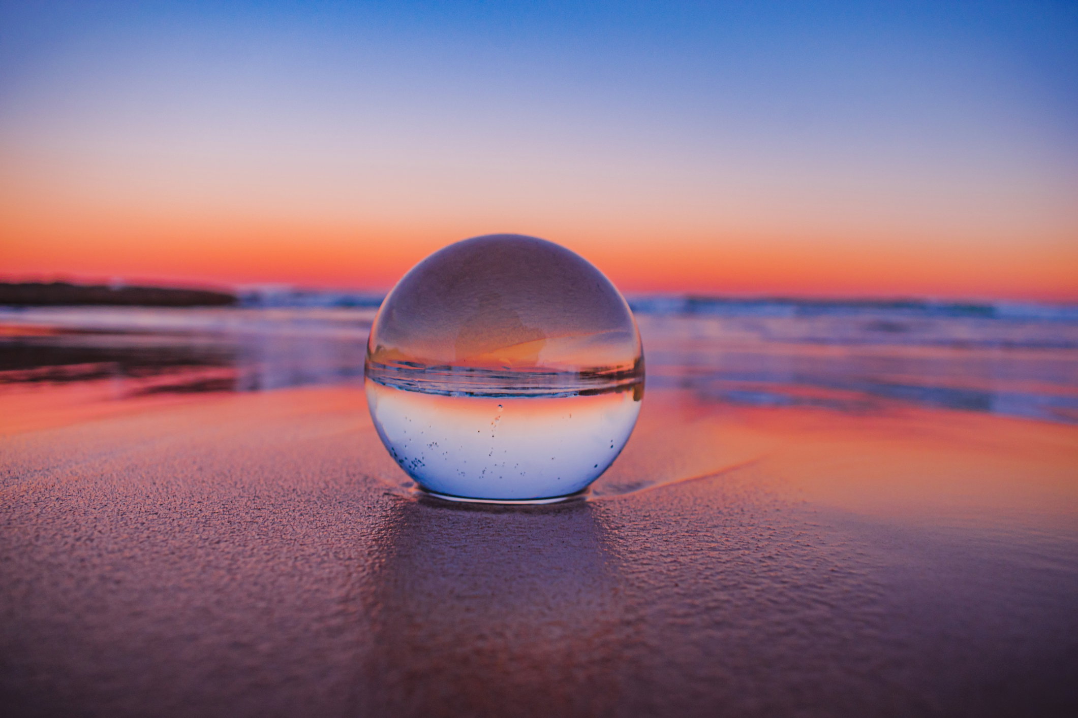 Mesmerizing view of a clear crystal ball placed on the sand near the beach during the sunset