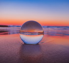 Mesmerizing view of a clear crystal ball placed on the sand near the beach during the sunset