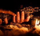 In the hands of the witches bunch of dry herbs for divination. The light from the candles on the old magic table. Attributes of occultism and magic
