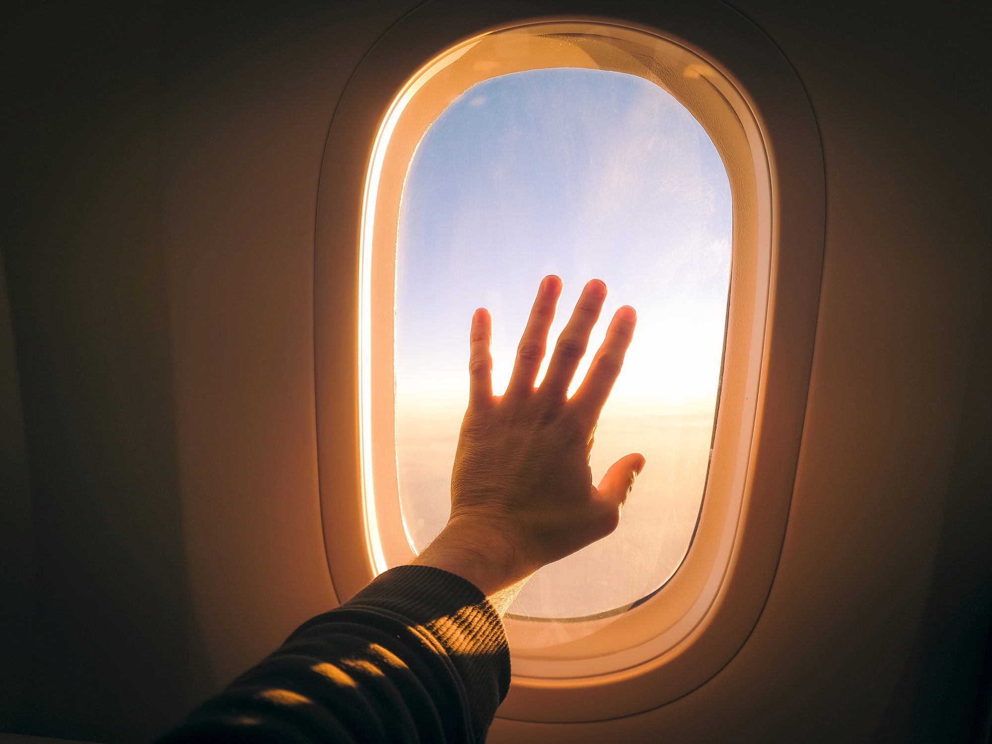 Touching plane window while flying in the sky during sunset