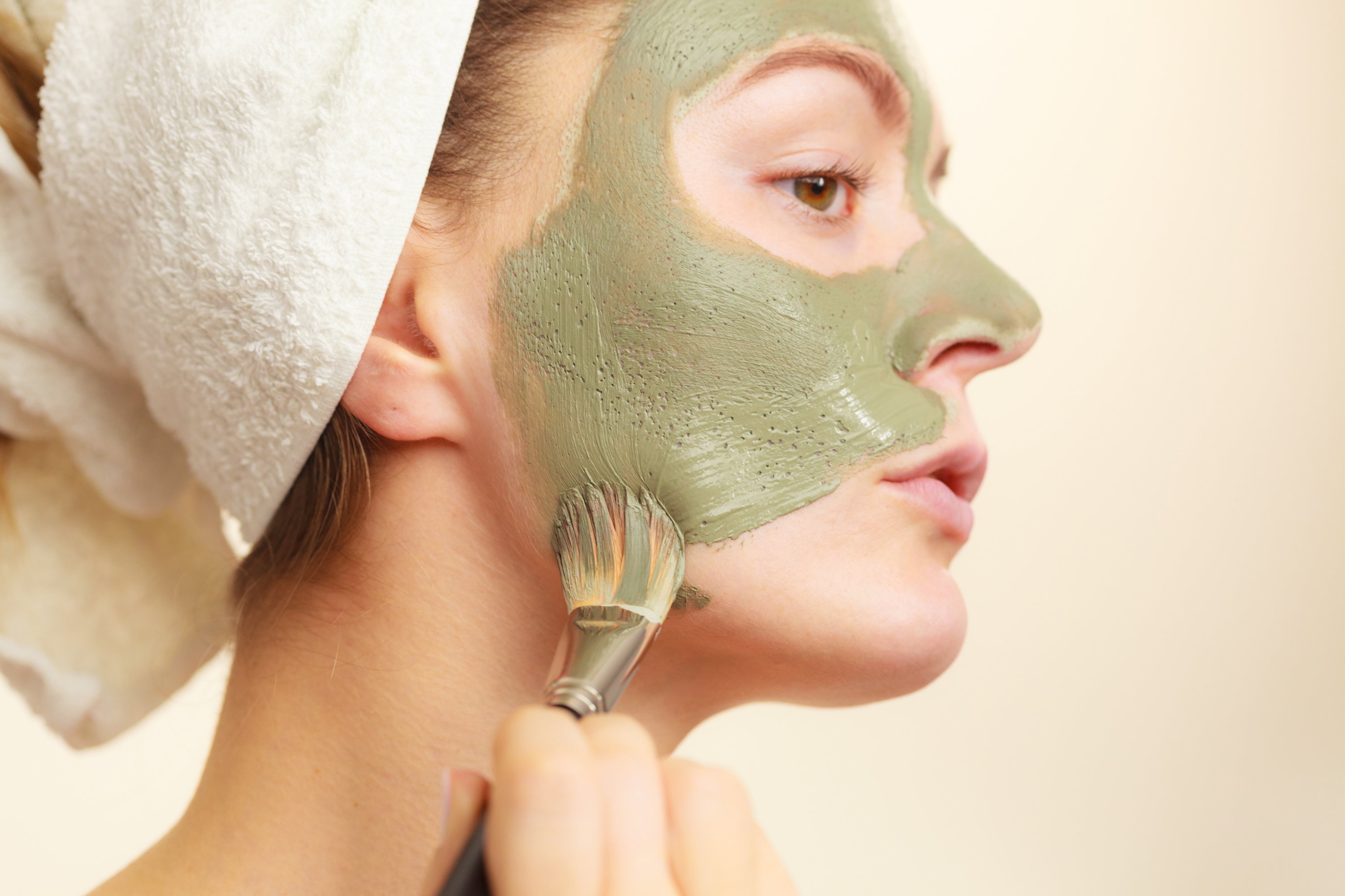 Woman applying with brush clay mud mask to her face