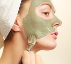 Woman applying with brush clay mud mask to her face