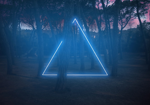 Blue neon triangle light between pine trees with futuristic visual effect.