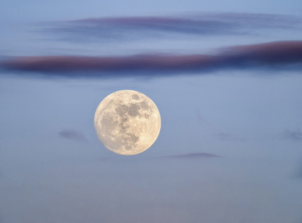 Full frame of the full moon at blue hour with a blue sky and some high clouds