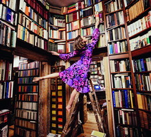 Carefree woman on ladder reaching for book in library
