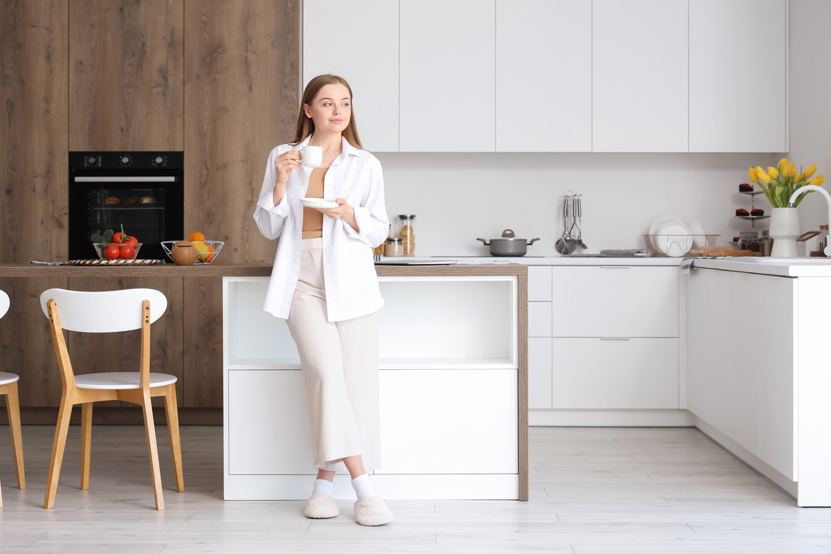 Happy young woman enjoying cup of coffee in modern kitchen