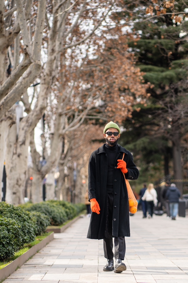 Stylish bearded black man walking on sidewalk wear sunglasses gloves holding string bag with oranges