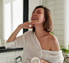 Woman laughing while applying cream while standing in the bathroom