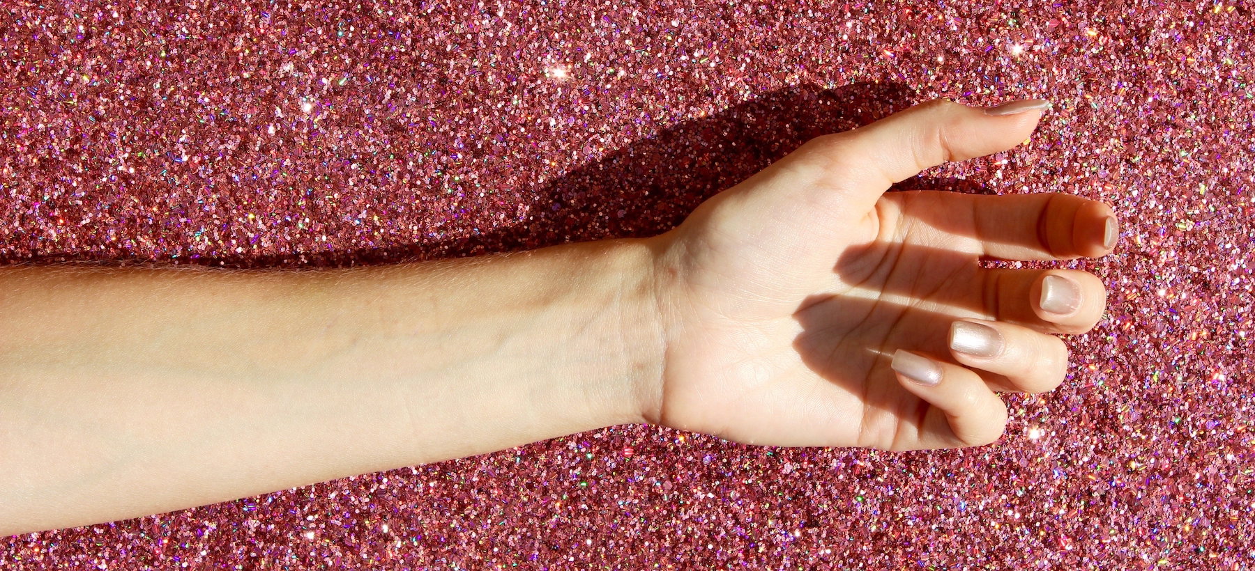 Cropped Image Of Hand Over Pink Glitter On Sunny Day