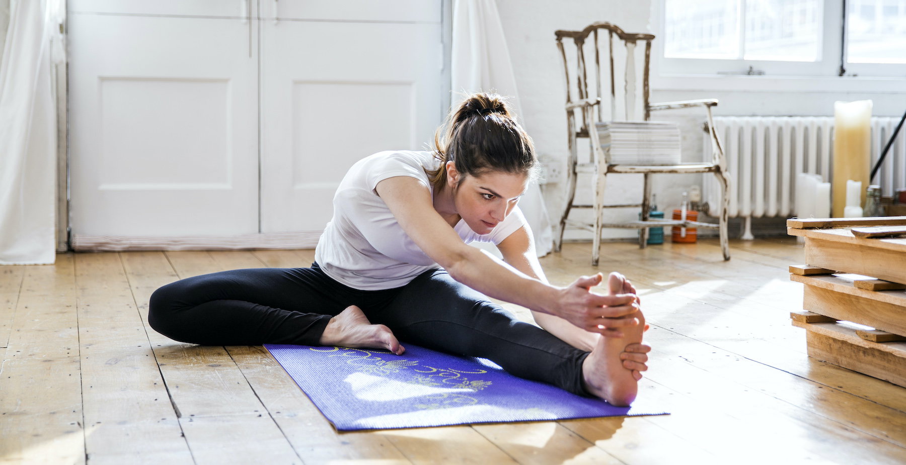 Young woman practicing yoga, touching toes in apartment