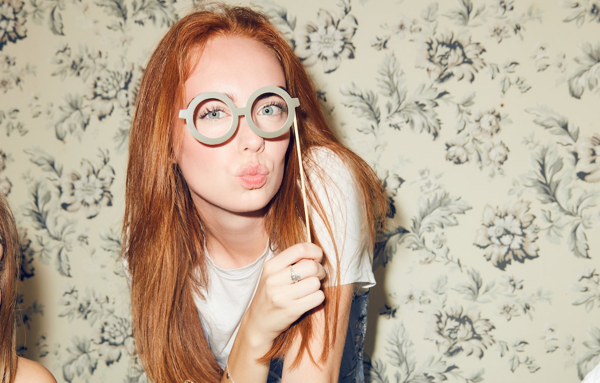 Portrait of young redhead woman holding eyeglasses prop while sitting amidst friends during dinner party at home