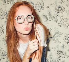 Portrait of young redhead woman holding eyeglasses prop while sitting amidst friends during dinner party at home