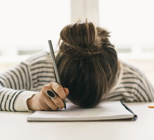 Woman writing on notepad resting her head on table