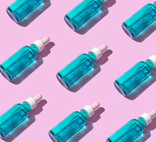 Transparent liquid dropper and blue bottle on pink pastel background