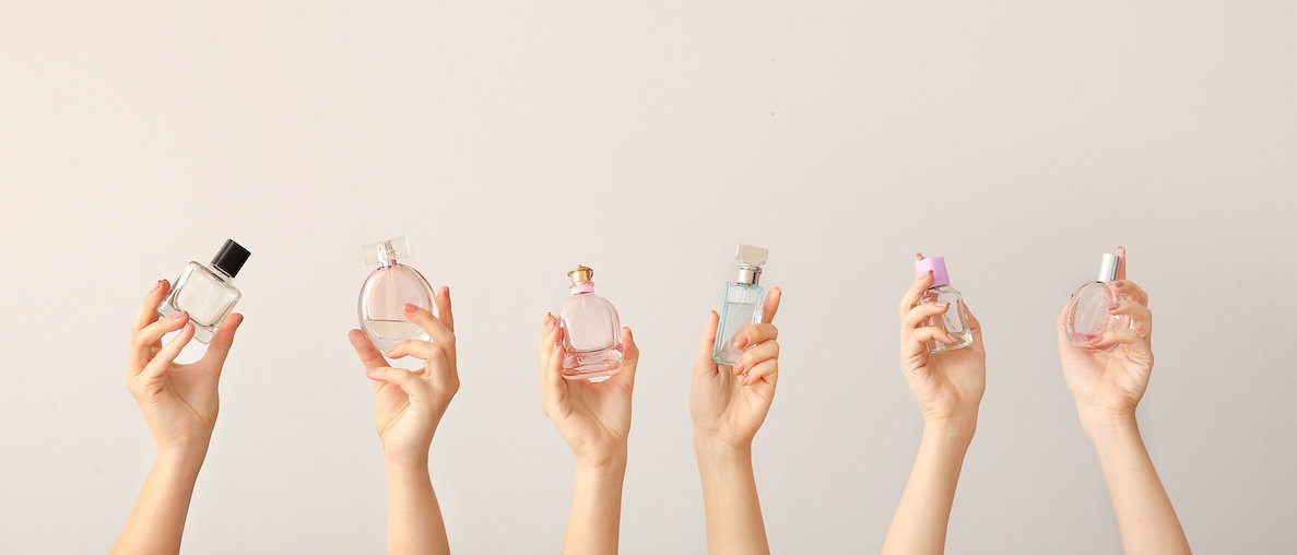 Female hands with different perfume bottles on grey background