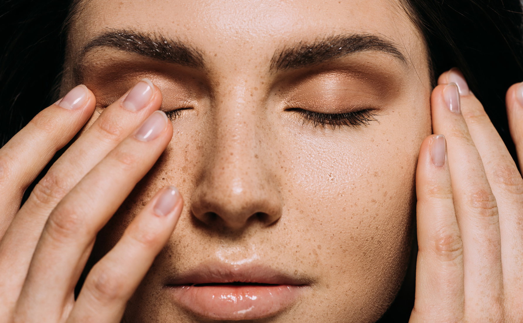 close up view of tender girl with freckles on face touching closed eyes
