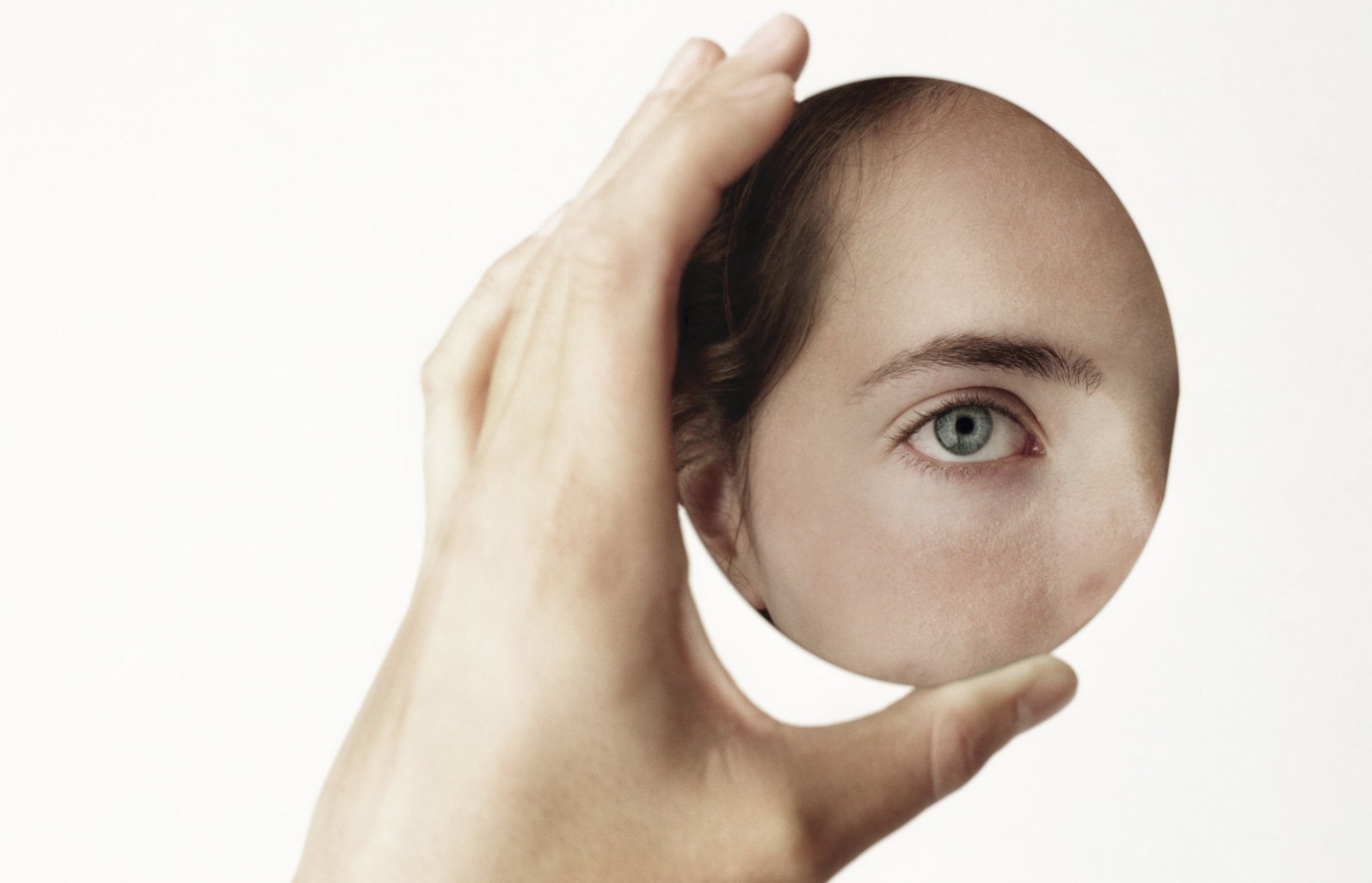 Young woman holding oval mirror, face reflected in mirror, close-up