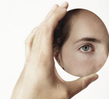 Young woman holding oval mirror, face reflected in mirror, close-up