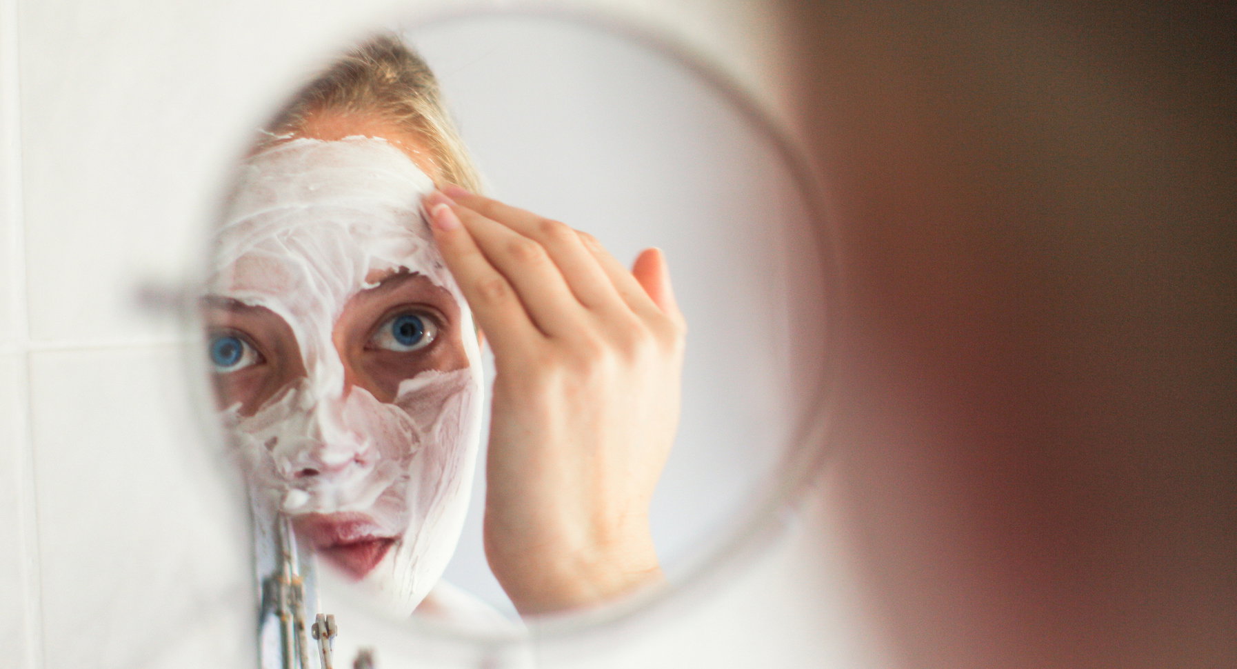a Young woman with blue eyes applying a beauty mask.