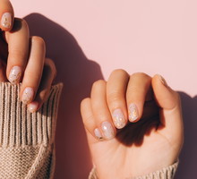 Glowing hands in sweater with knitted sleeves and with nude color manicure with gold particles on pink table. Trendy colors of the year