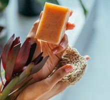 Woman hands holding natural organic solid green soap bar made with olive oil on blue background. Healthy lifestyle, beauty, skin care. Zero waste home concept.