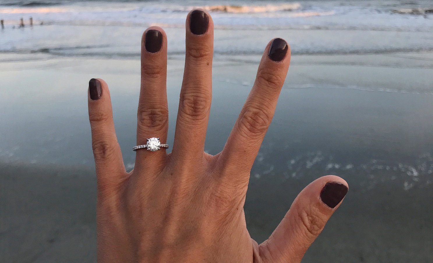 Cropped Hand Of Woman Showing Wedding Ring At Beach Against Sky During Sunset