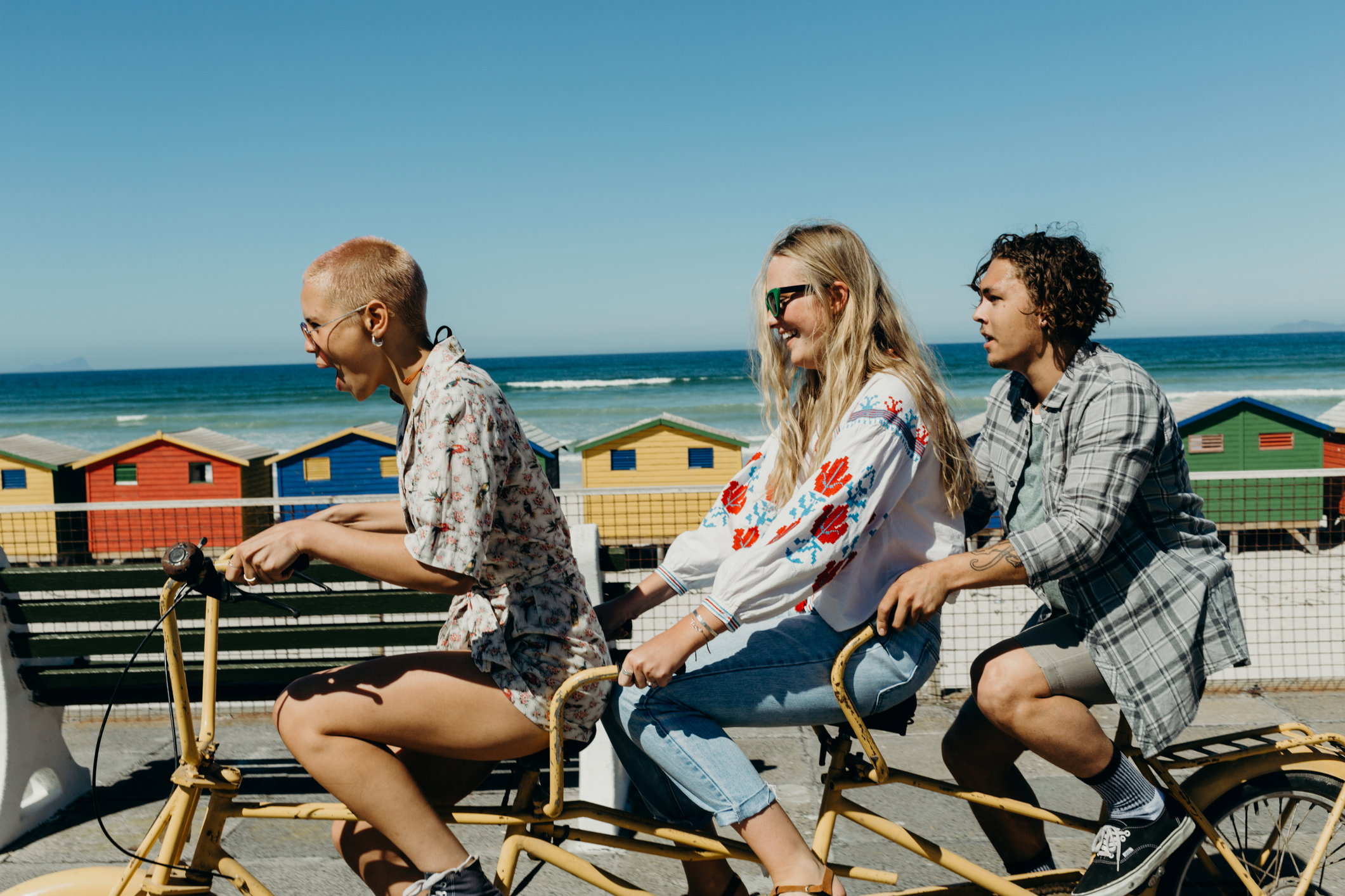 Three friends laughing on a tandem bicycle on a boardwalk