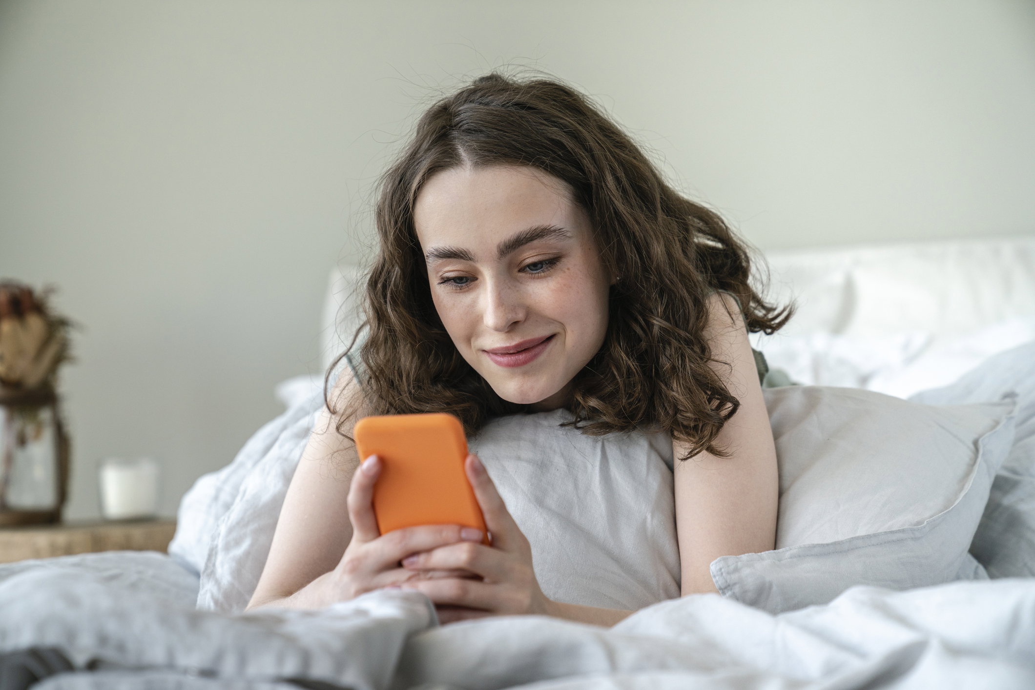 Smiling young woman using mobile phone on bed at home