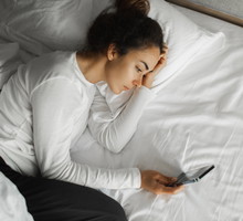 Sad woman lying in bed with phone and watching on social media. Gadget addiction