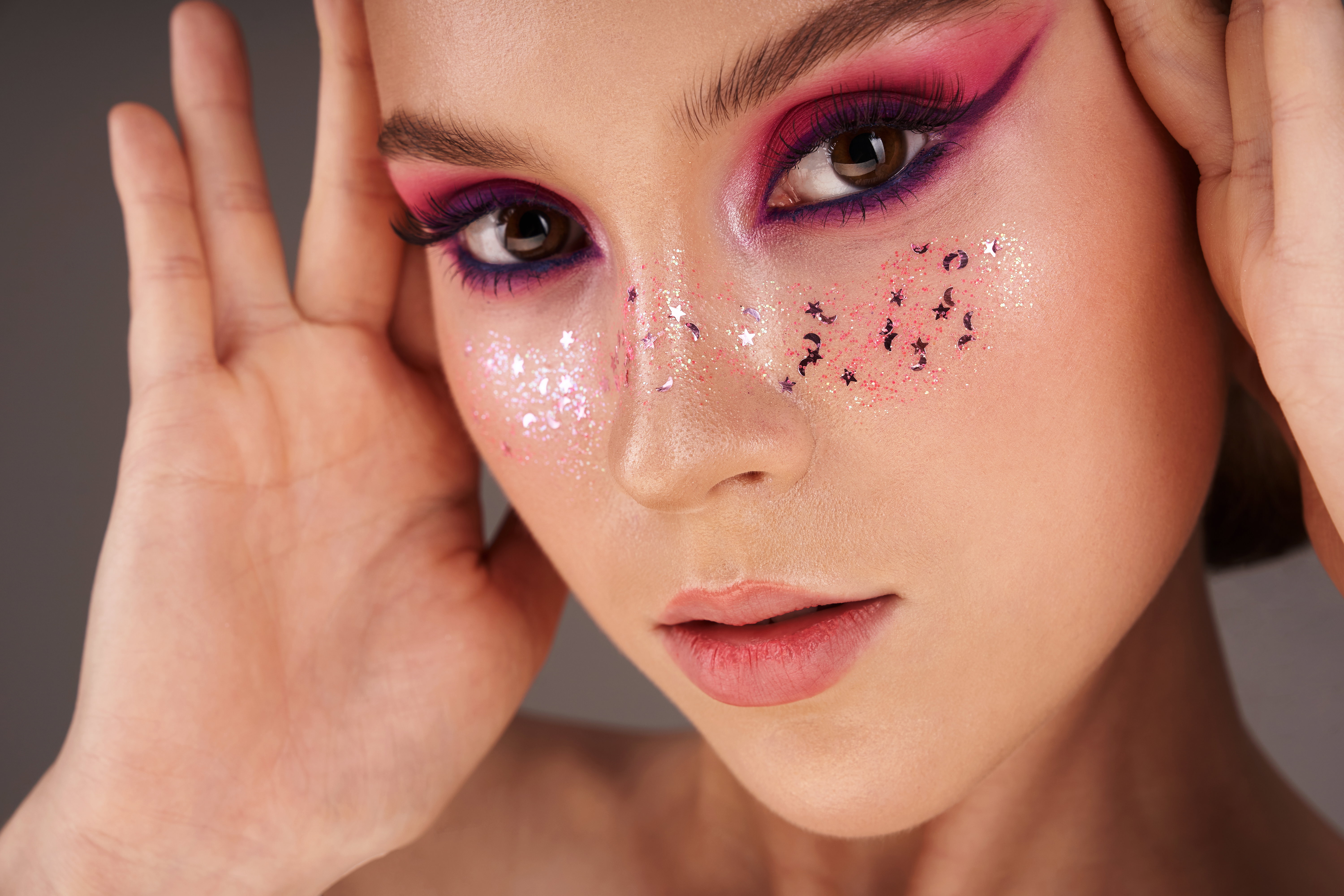 Beauty closeup portrait of a young woman with pink eyeshadow and glitter on the face.