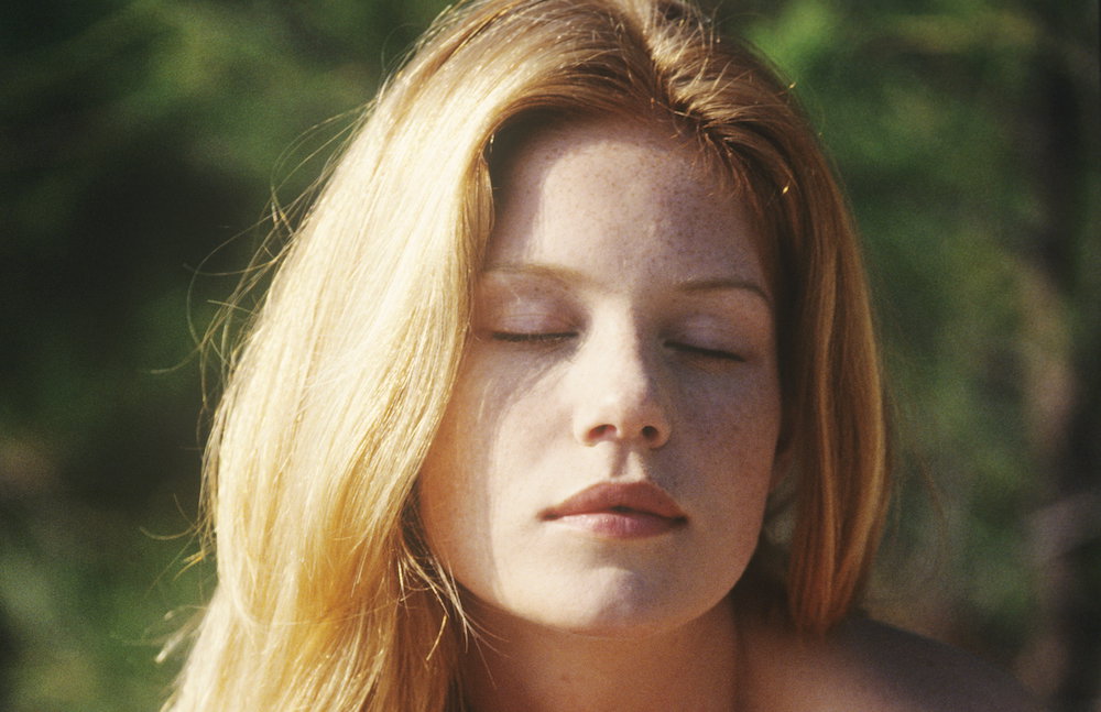 Portrait of a young woman sitting outdoors, sunbathing