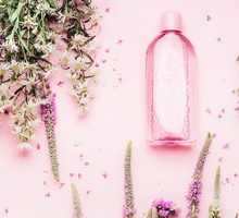 Natural cosmetic products setting with various bottles and fresh herbs and flowers on pink background, top view, flat lay. Beauty, skin, hair or body care concept