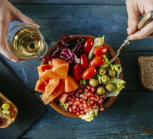 Close-up of woman's hands eating salad wit tomato, pomegranate, papaya and olives, papaya with fruits and with wine glass