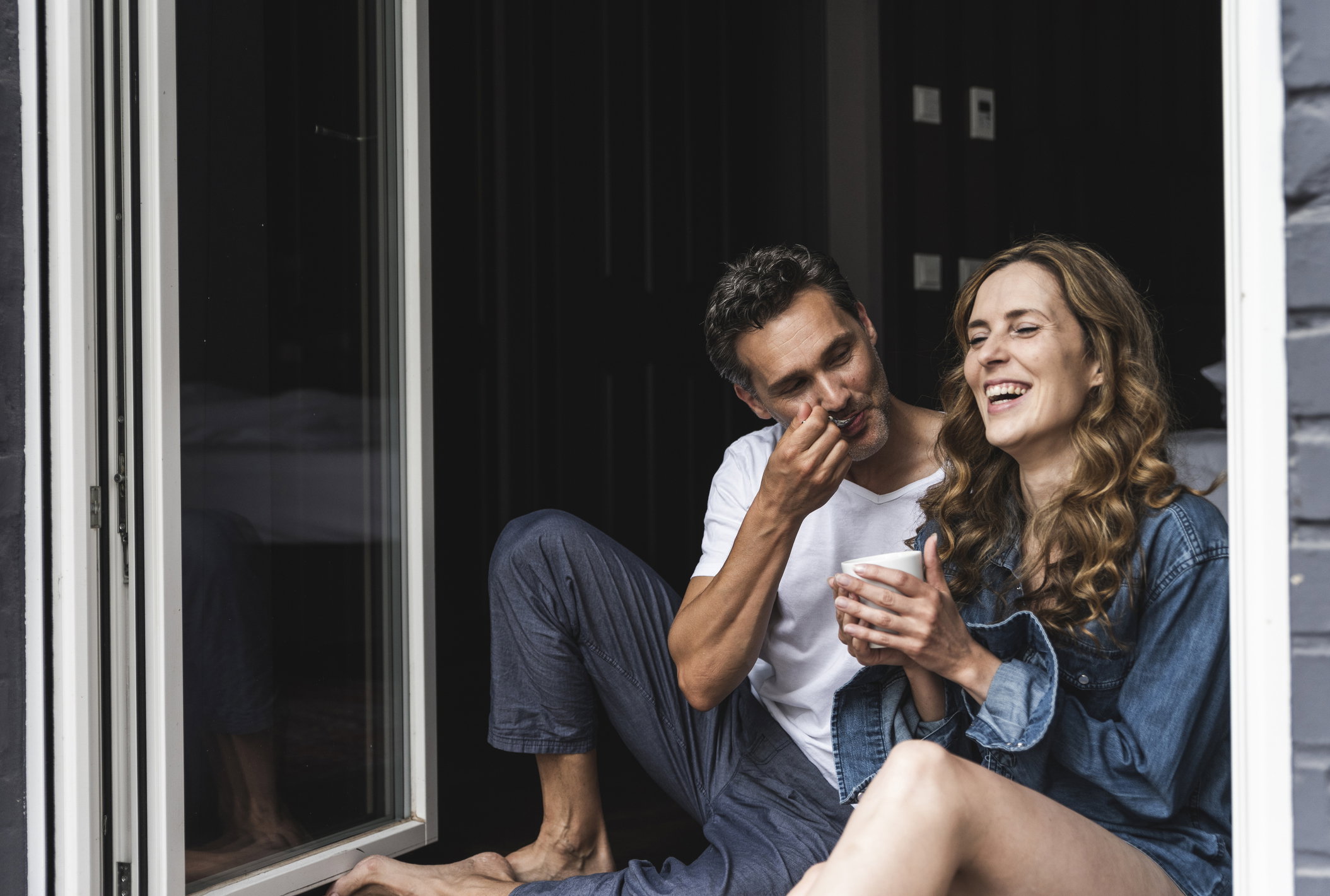 Happy couple in nightwear at home sitting at French window