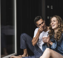 Happy couple in nightwear at home sitting at French window