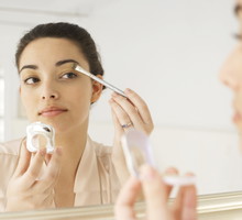 Young woman applying make-up in mirror, using brush, close-up