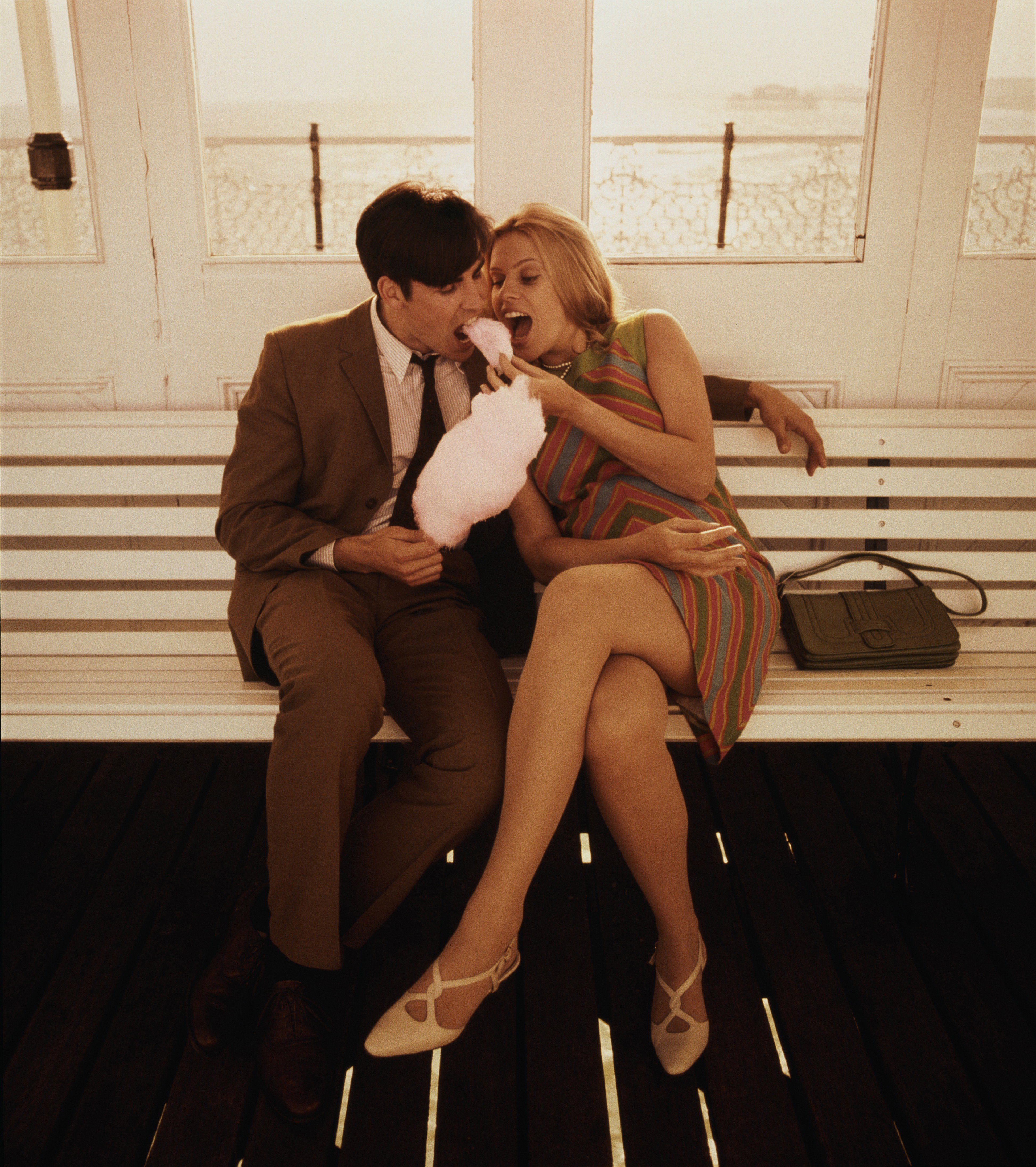 Young couple sitting on bench, eating candyfloss (Enhancement)