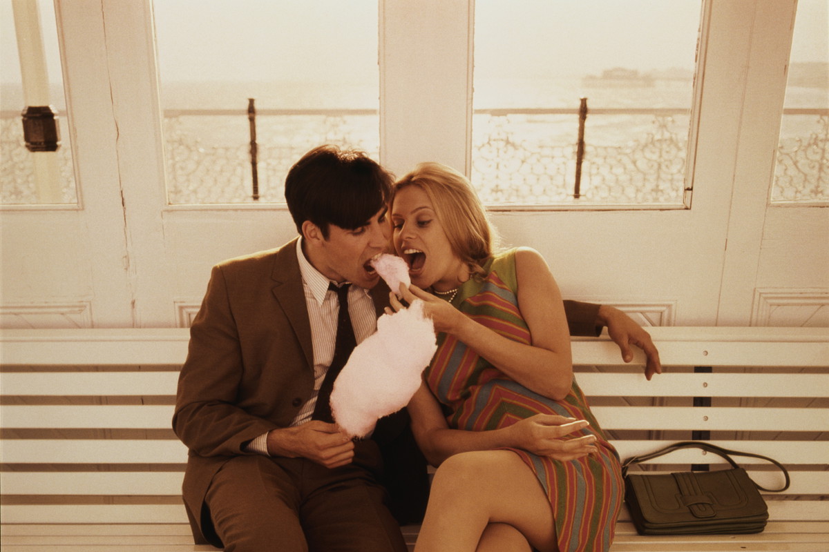 Young couple sitting on bench, eating candyfloss (Enhancement)