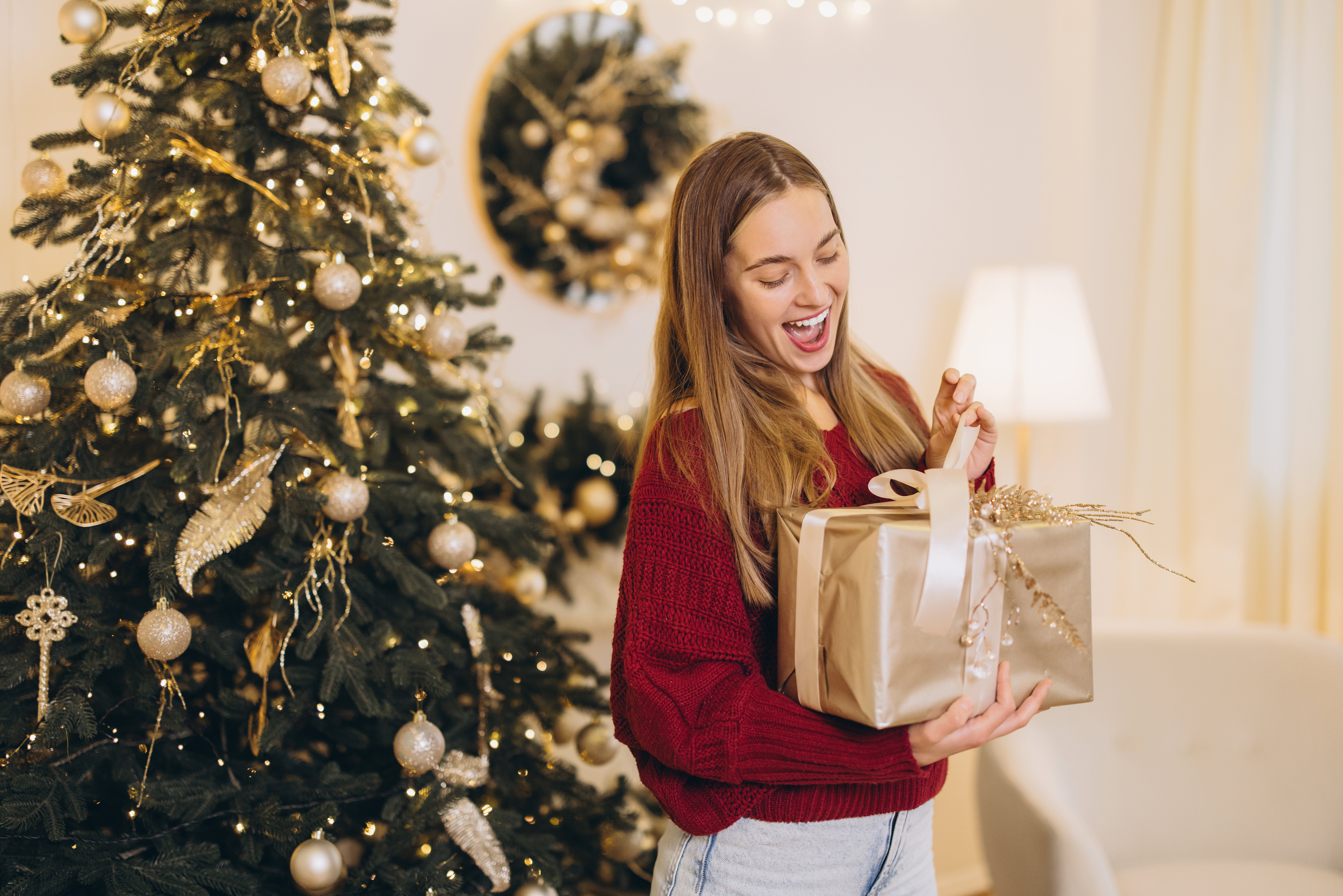 Excited woman opening christmas gift near decorated tree