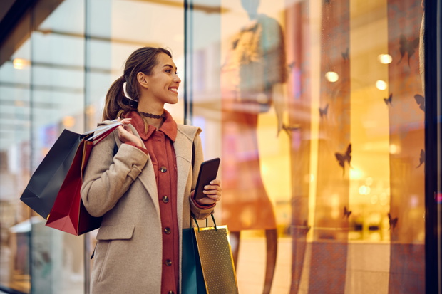 Happy woman with shopping bags looking at store windows while walking through city.