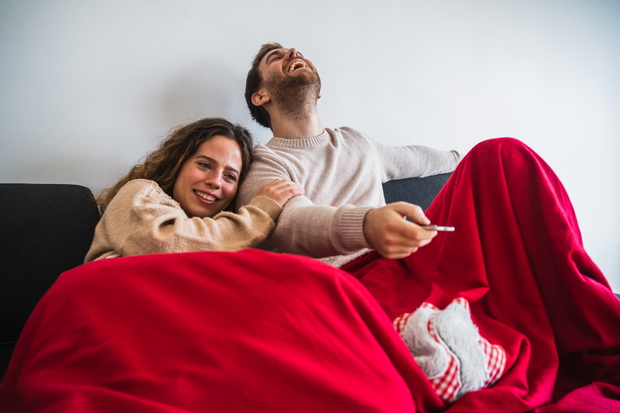 Cheerful man and woman watching TV covered with blanket